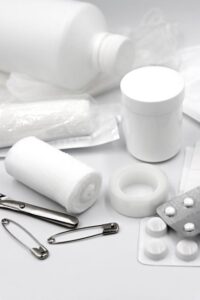 A household first-aid container, digital thermometer, gauze, gloves, medications, and blood pressure monitor arranged on a kitchen table.