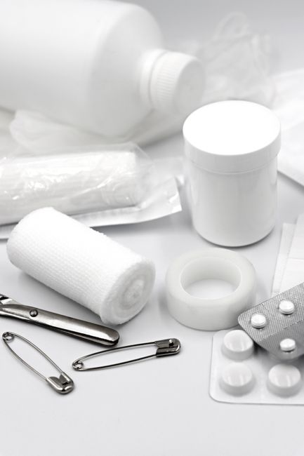A household first-aid container, digital thermometer, gauze, gloves, medications, and blood pressure monitor arranged on a kitchen table.